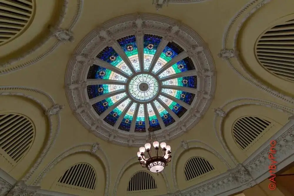 The ornate circular stained glass dome features intricate blue, green, and white patterns set within a detailed white stone frame.