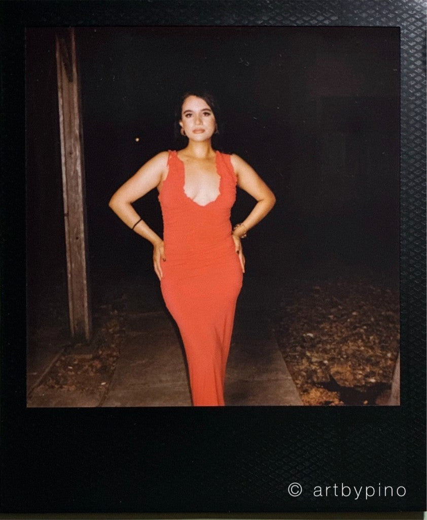 Mujer con un vestido largo rojo, con las manos en las caderas, en una acera de noche junto a un poste de madera desgastado, enmarcada en una Polaroid negra — Polaroid Color i-Type Black toma Edition, Polaroid I-2