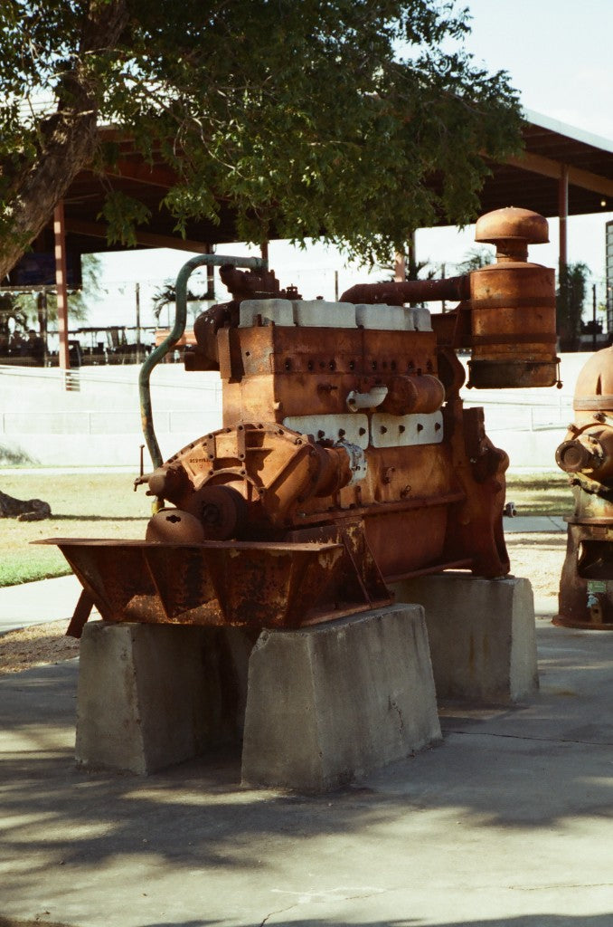 35mm + Reflx Lab 320D AHU (Kodak Vision 3 250D 5207 AHU, C-41) — Motor histórico oxidado sobre bloques de hormigón en la estación de bombeo y parque de bomberos McAllen, McAllen, Texas