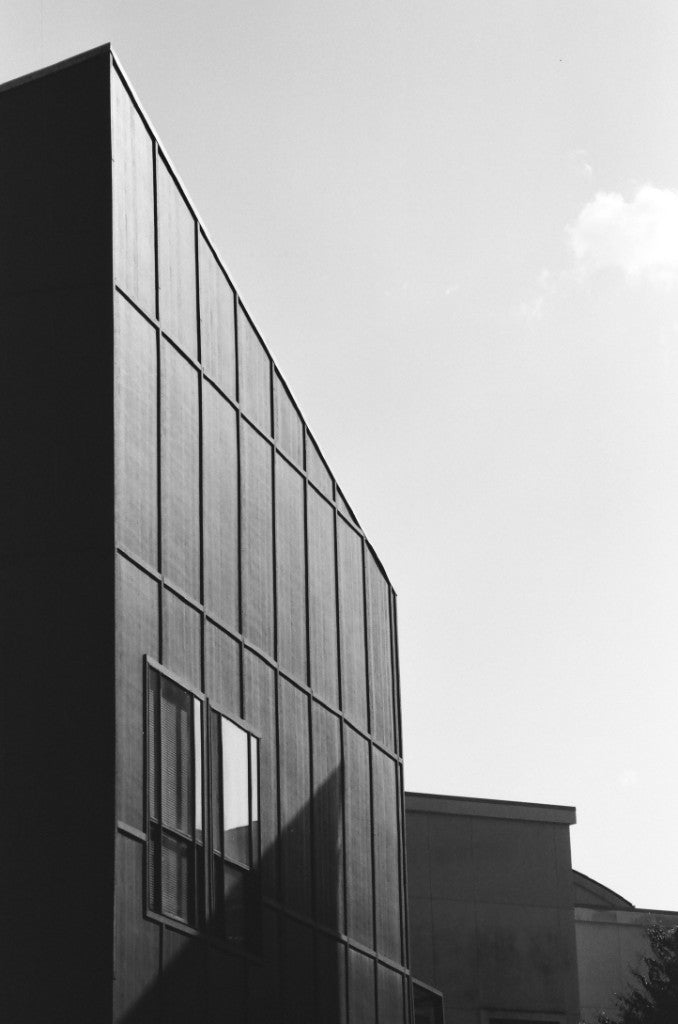 Modern building corner looking up at a geometric grid facade, shot on Reflx Lab Zarya 100 (Svema NK-2S) 35mm film, developed in D-76