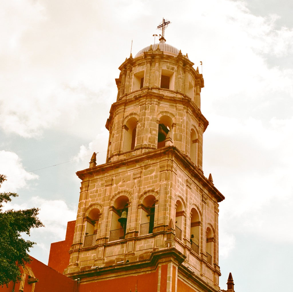 Stone bell tower and dome of Templo de San Francisco de Asís with orange-red lower walls, Santiago de Querétaro, shot on Silberra Color 160 120 film, developed in Kodak C-41