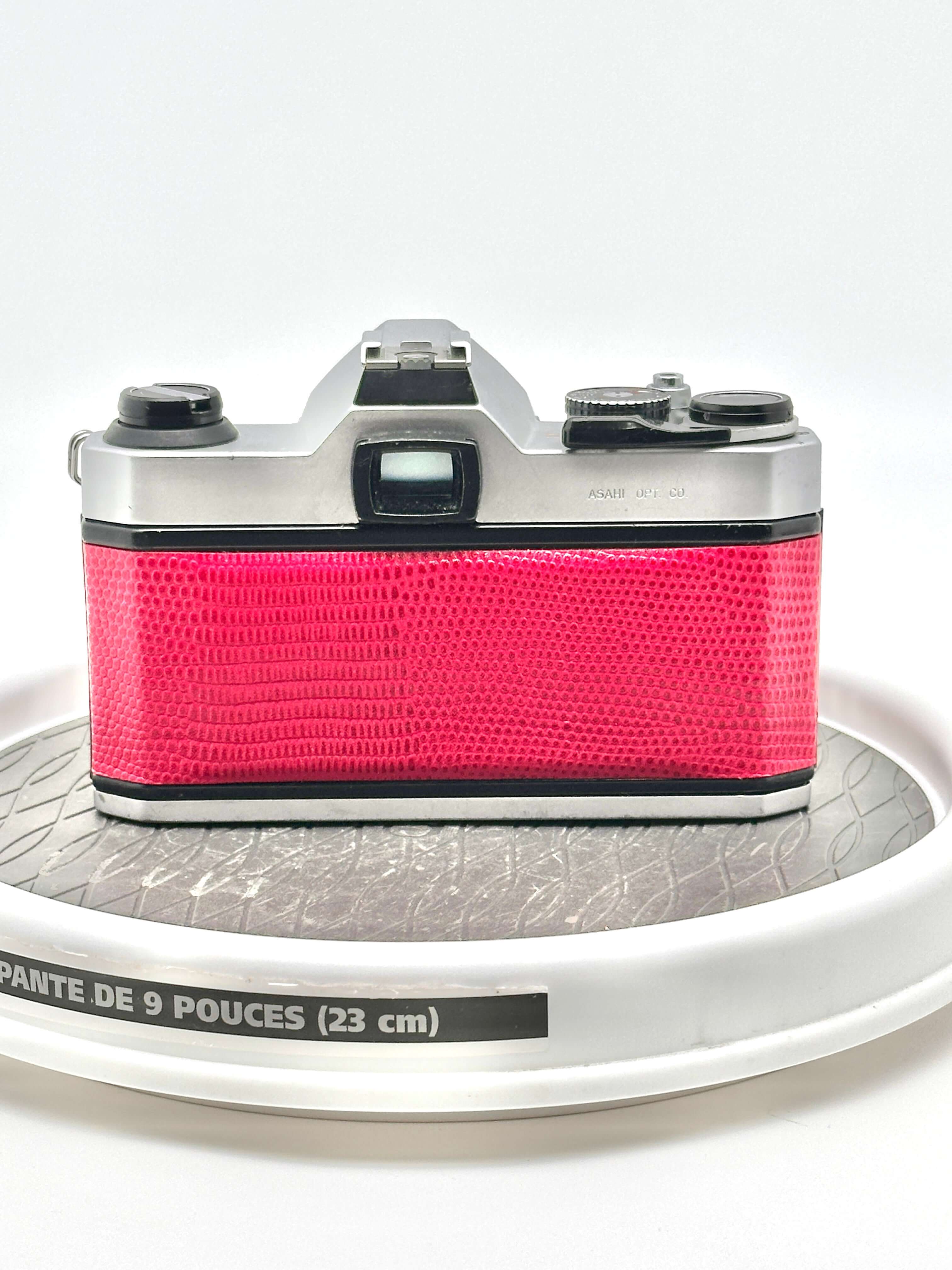 A vibrant pink camera with a textured, reptile-skin patterned body and silver metallic top plate.