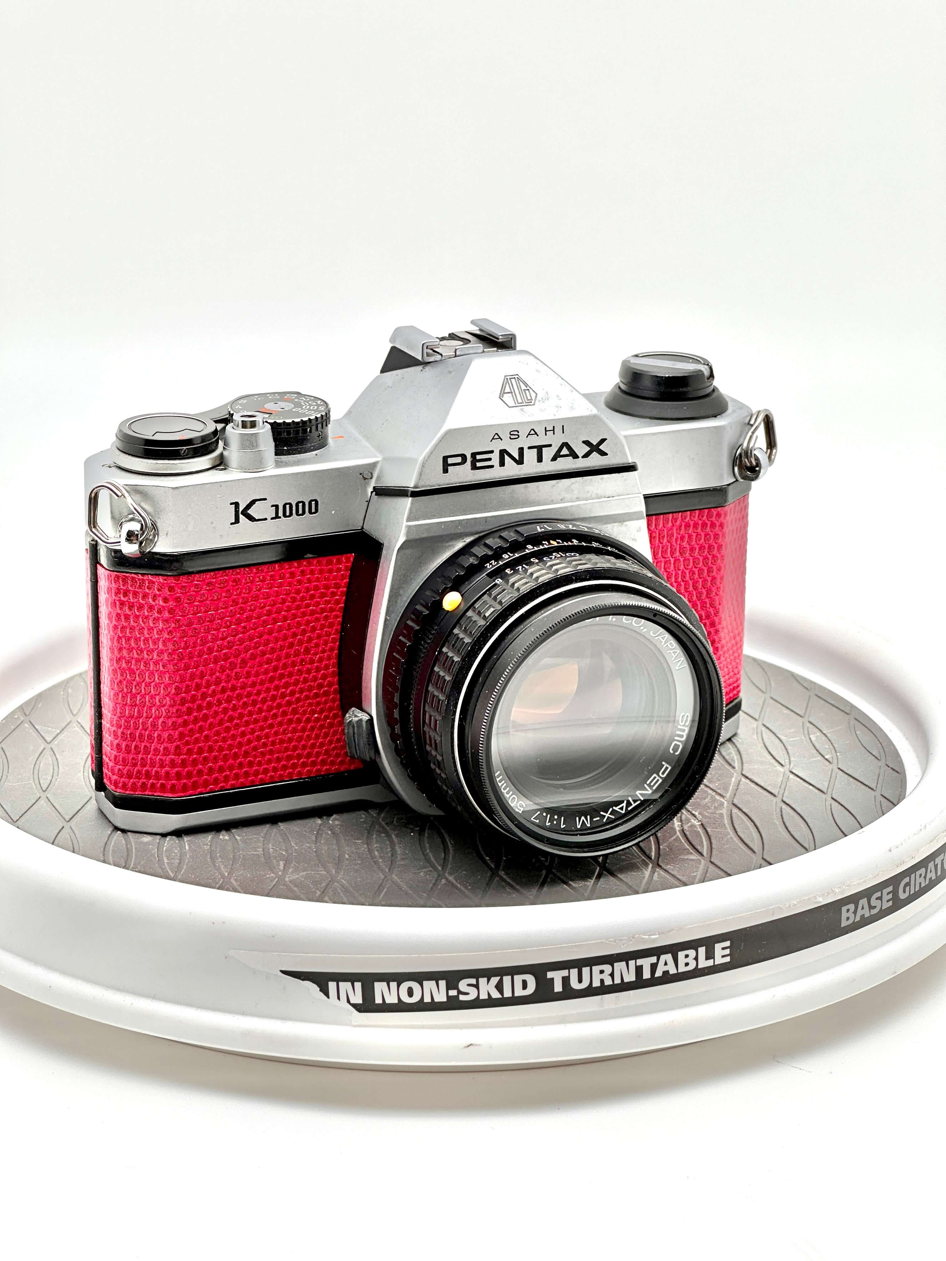 Silver and red asahi pentax k1000 film camera with textured leather grip.