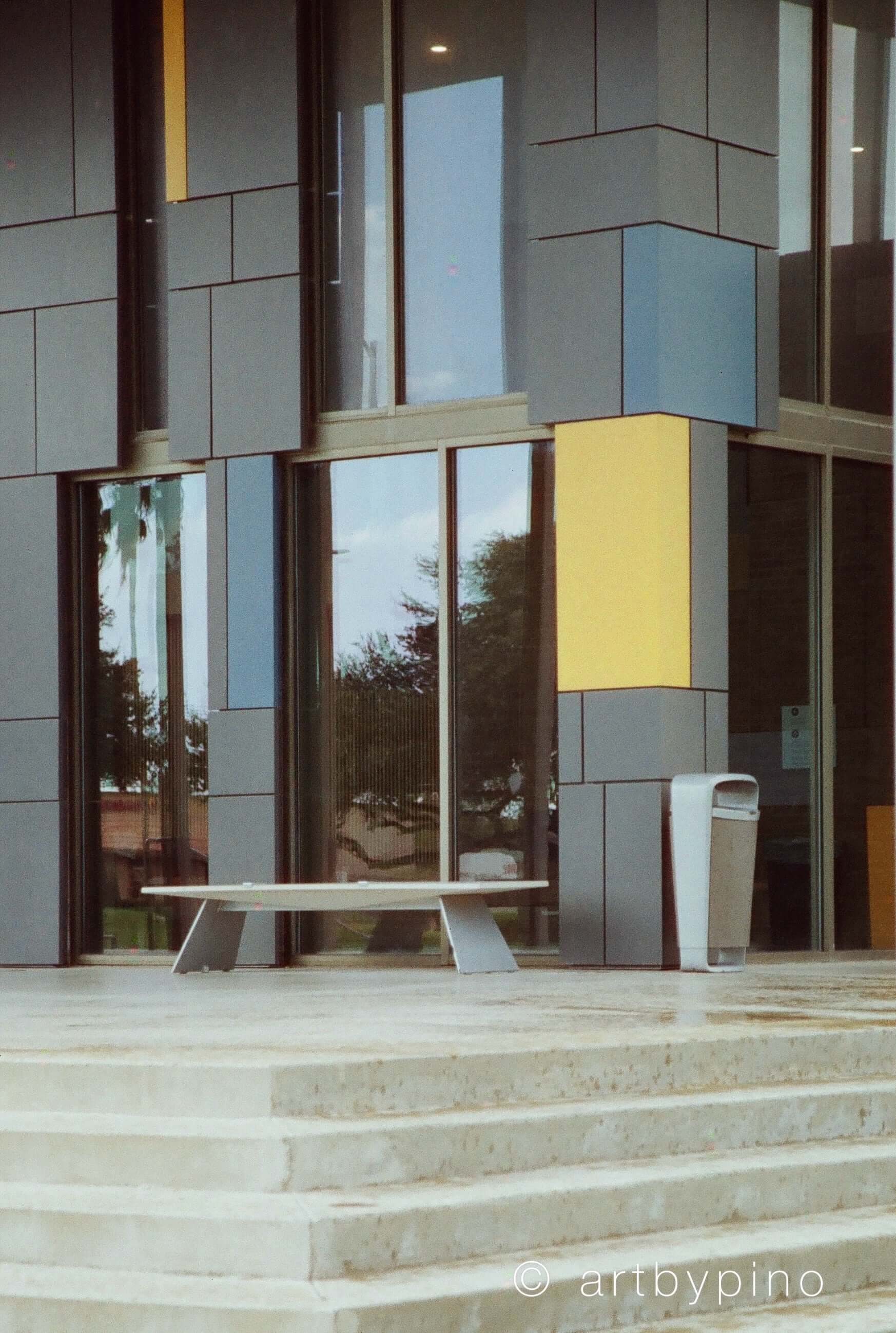 Modern minimalist bench with a sleek, light gray concrete surface and angular metal legs.