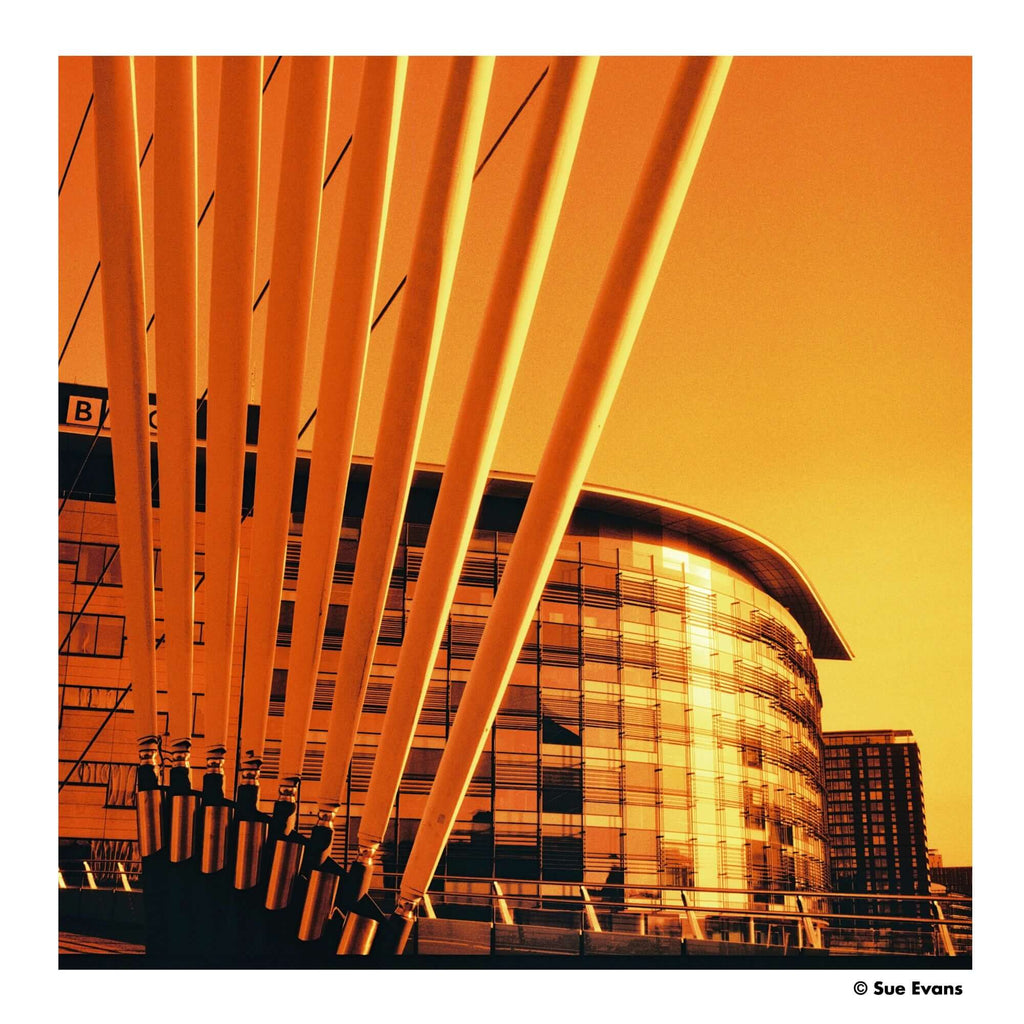 Golden-orange steel arches frame a modern glass building under a warm, sunlit sky.