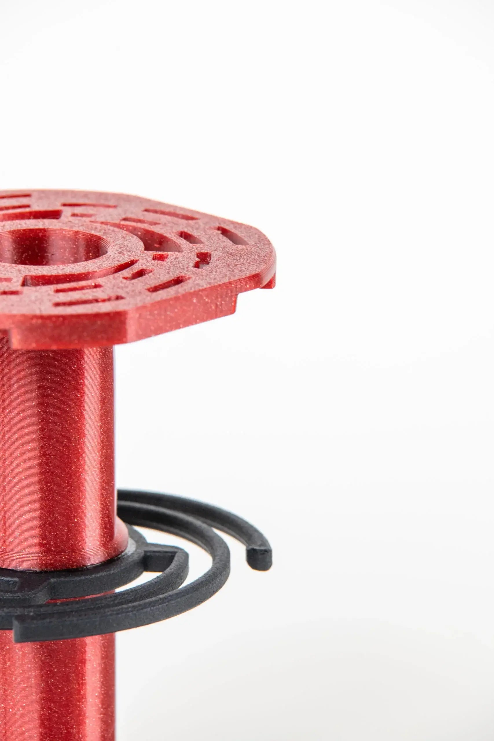 Red metallic spool with intricate cut-out pattern on top and black plastic rings wrapped around its base.