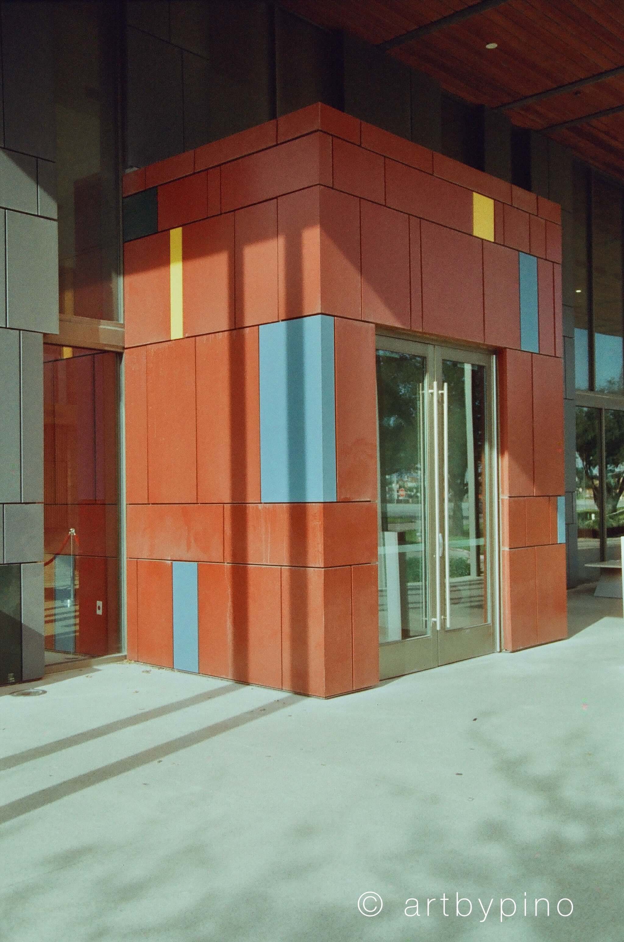 The building features a bold, geometric facade with reddish-orange panels accented by vertical stripes of yellow and blue.