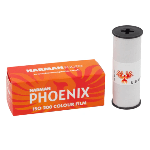 Harman phoenix iso 200 colour film in a vibrant orange box with fiery red and yellow swirls, packaged alongside its white cylindrical roll featuring an embossed phoenix logo.