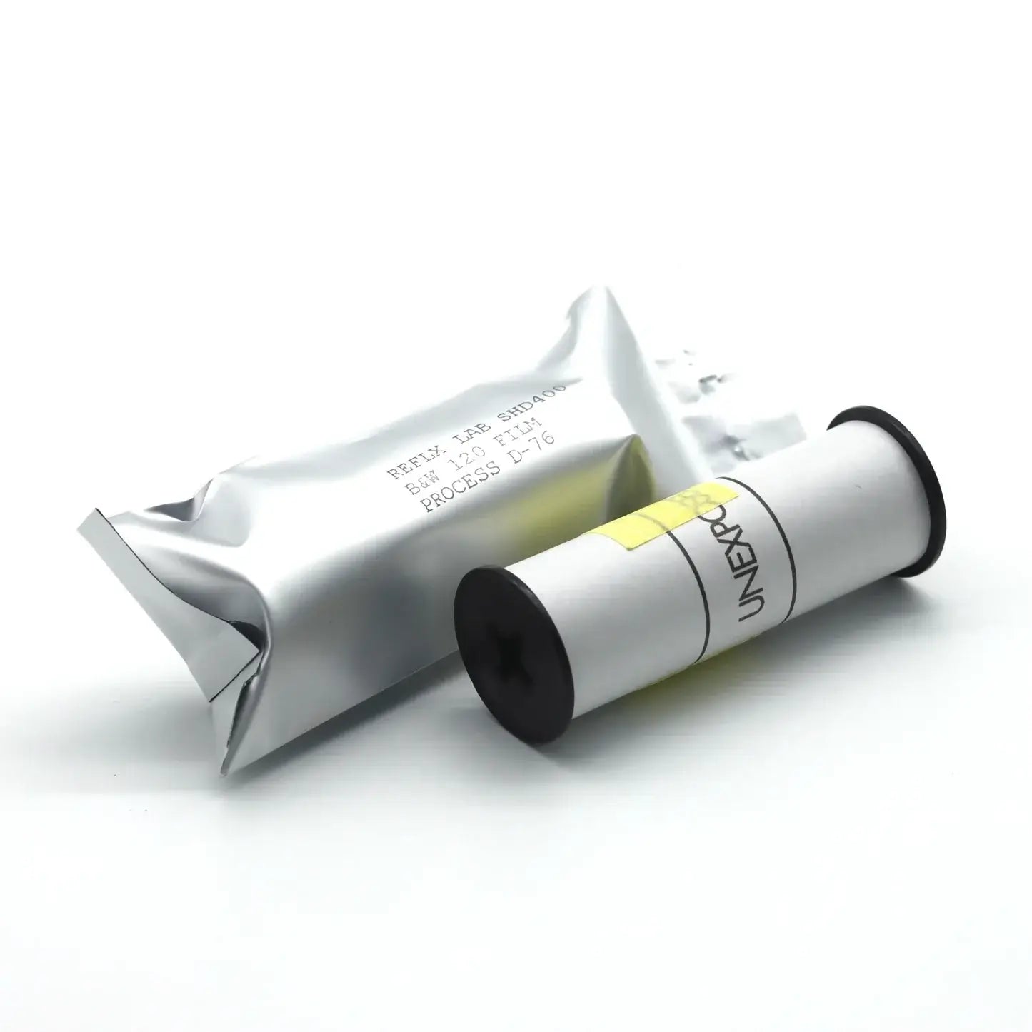 A white cylindrical film canister with black ends and a yellow label, branded ’uniexpo,’ resting beside its silver foil packaging.
