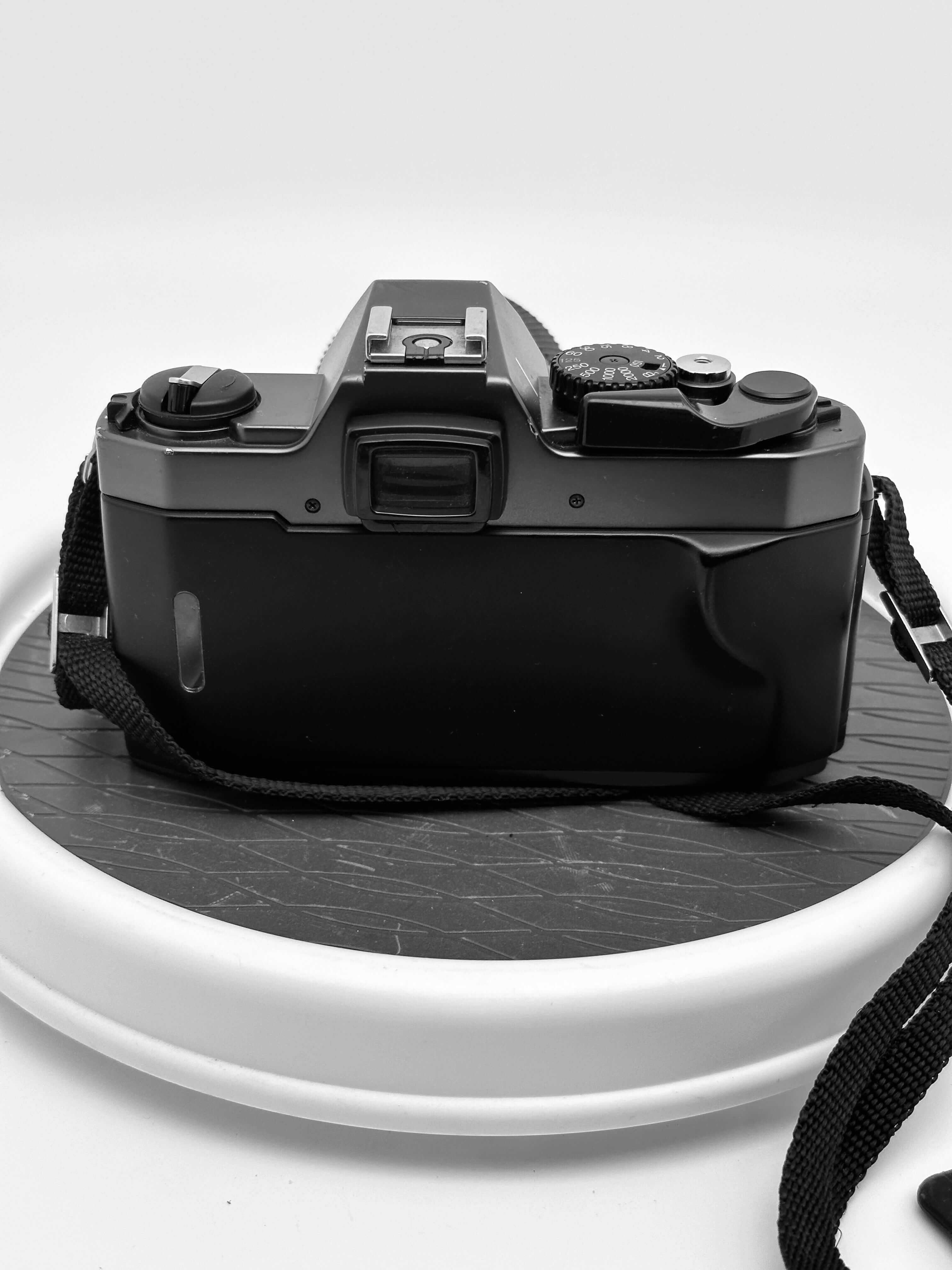 Black canon ae-1 film camera with a textured grip and attached strap.