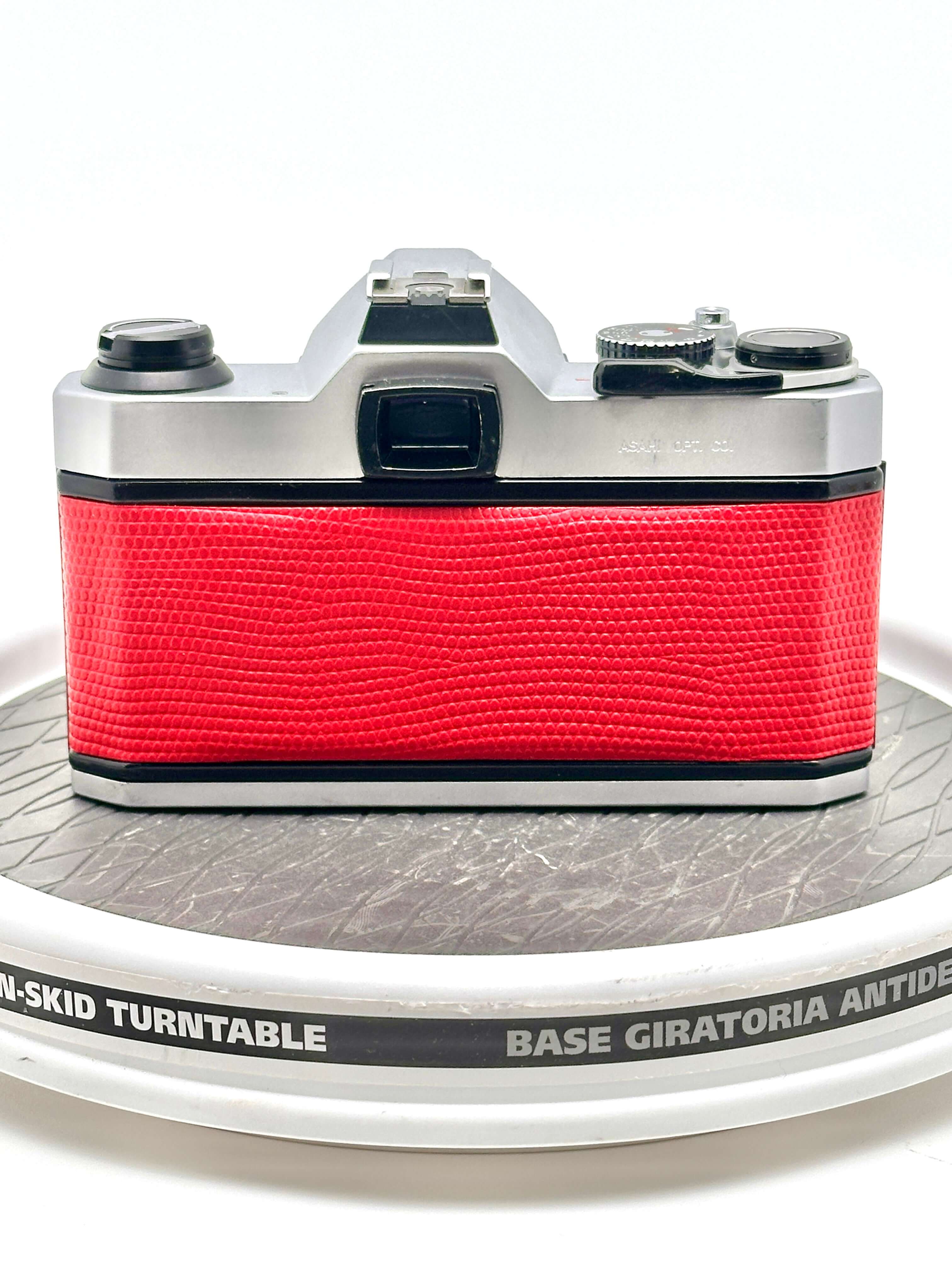 A vintage silver-bodied camera with a vibrant red textured leather grip.