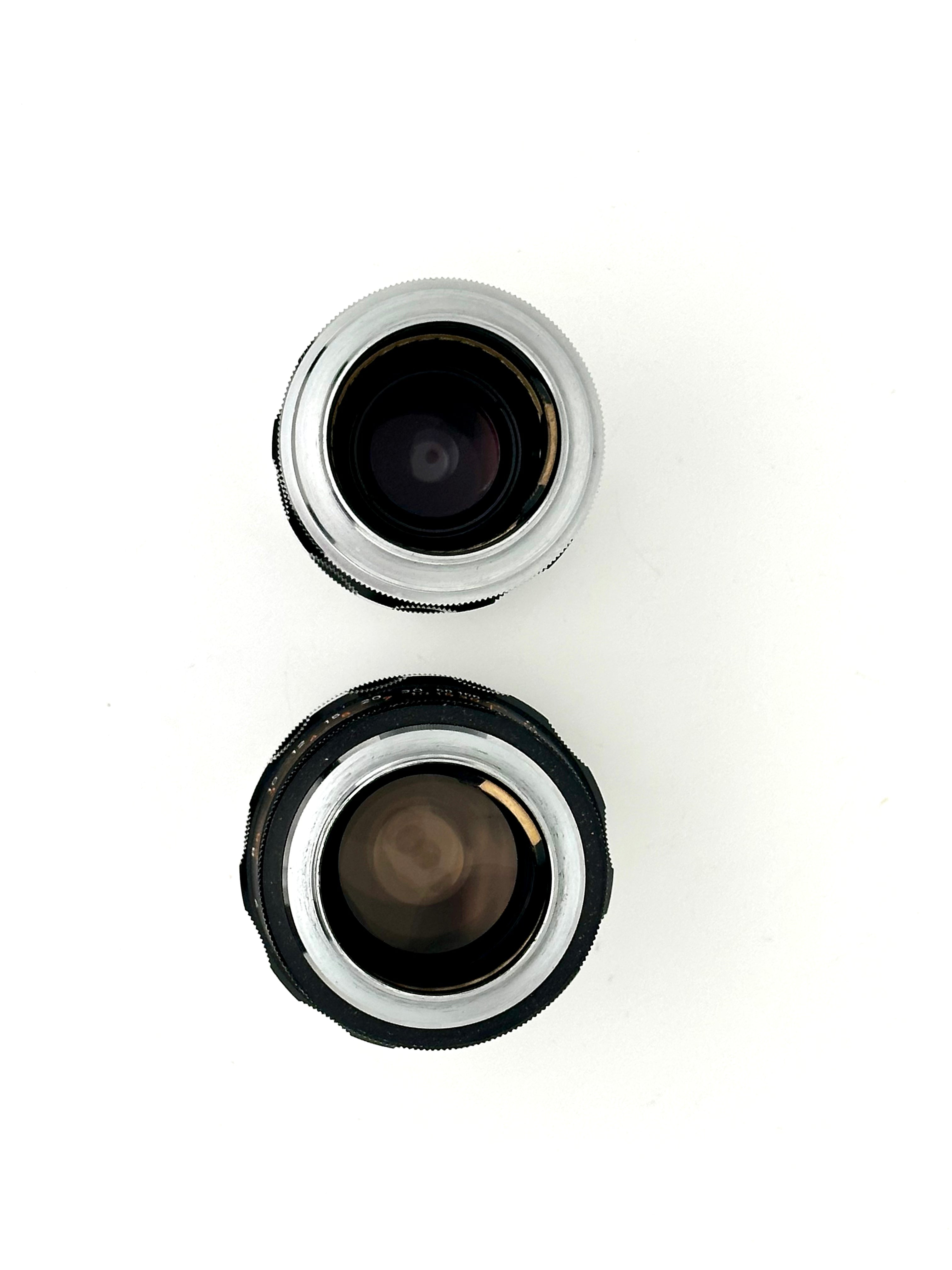 Two vintage camera lenses, one with a silver metallic rim and the other in black rubberized housing.