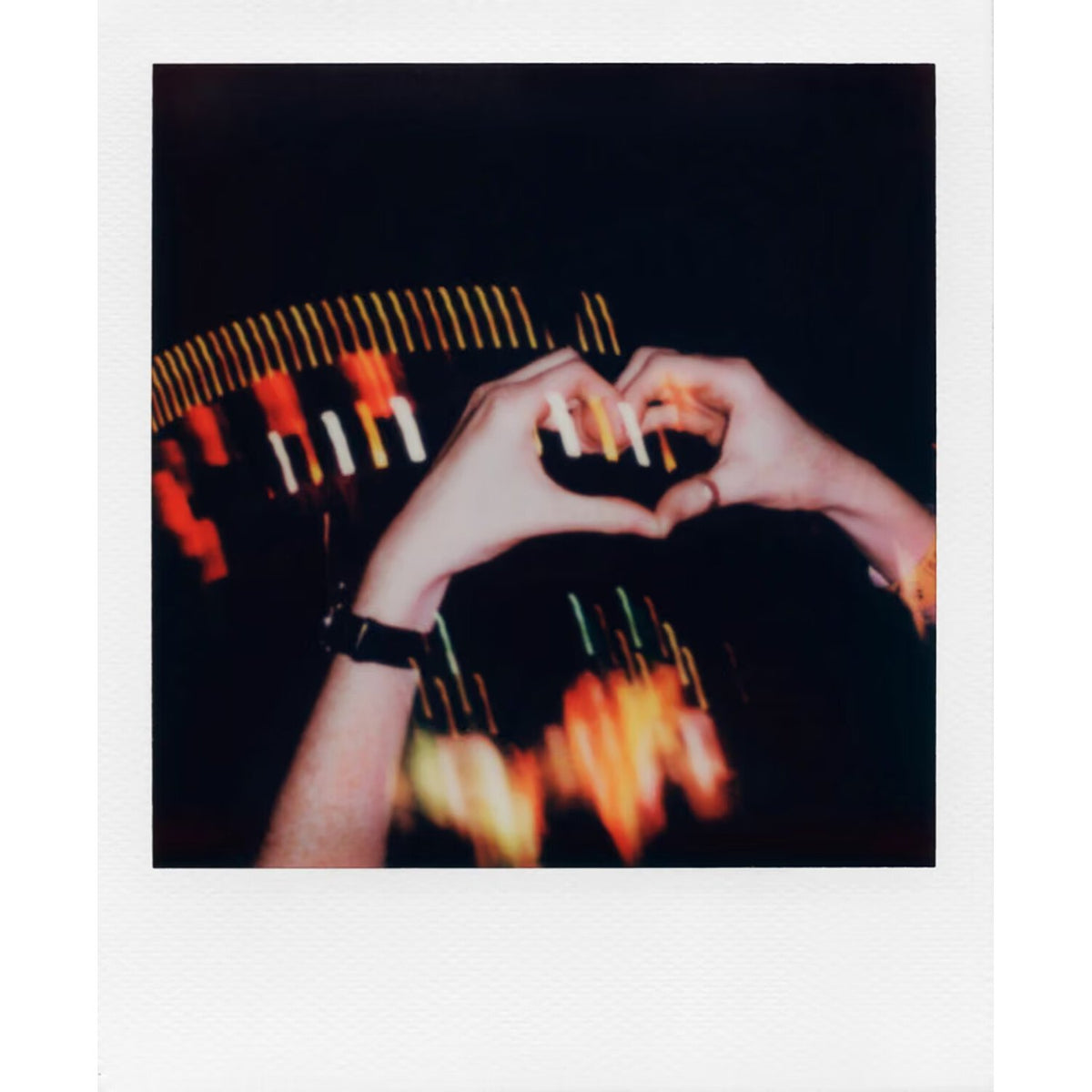 Instant photo of two hands making a heart over city lights, taken on Polaroid Go film