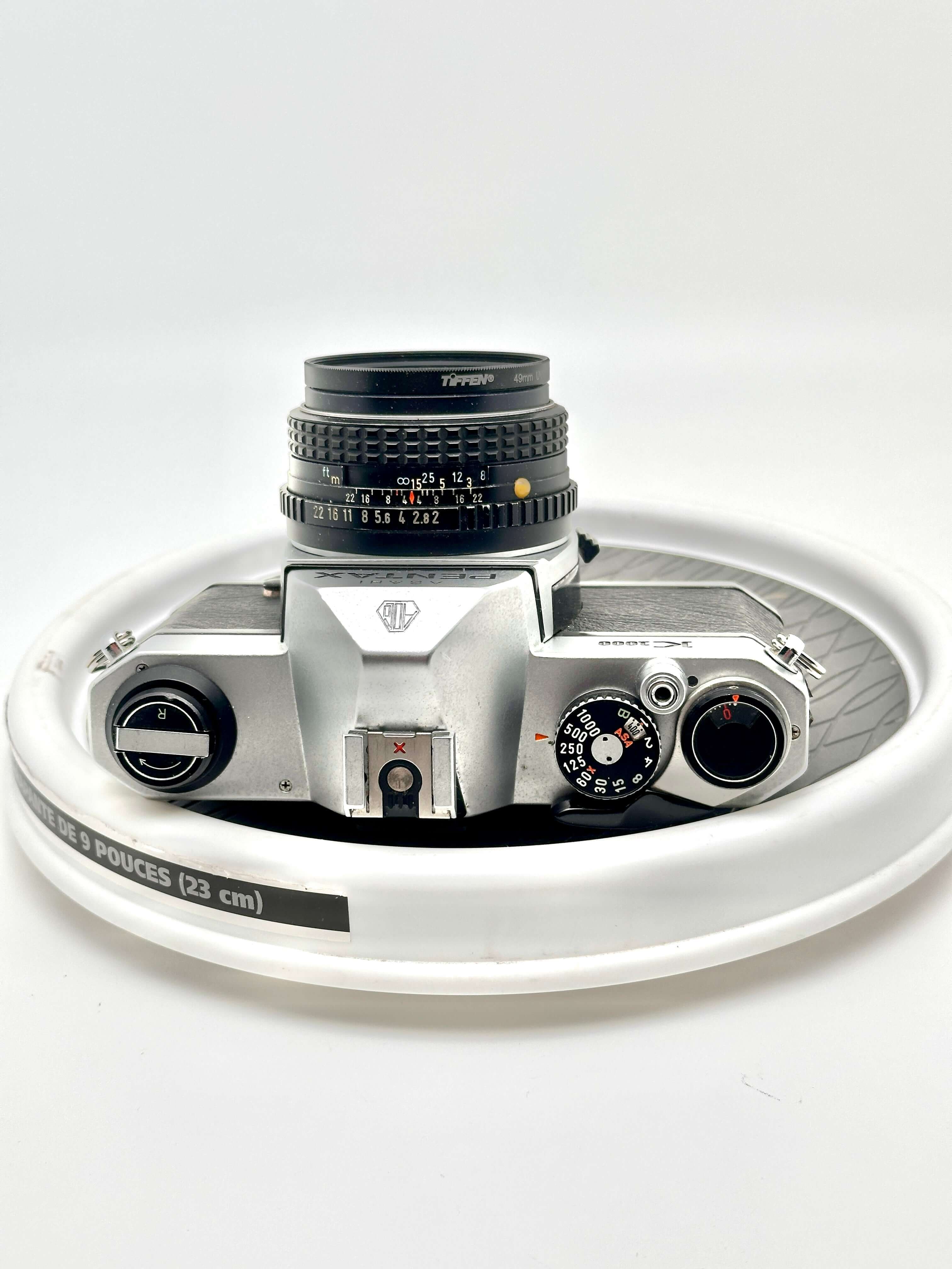 Silver-bodied canon ae-1 film camera with a black topcon lens mounted on top.