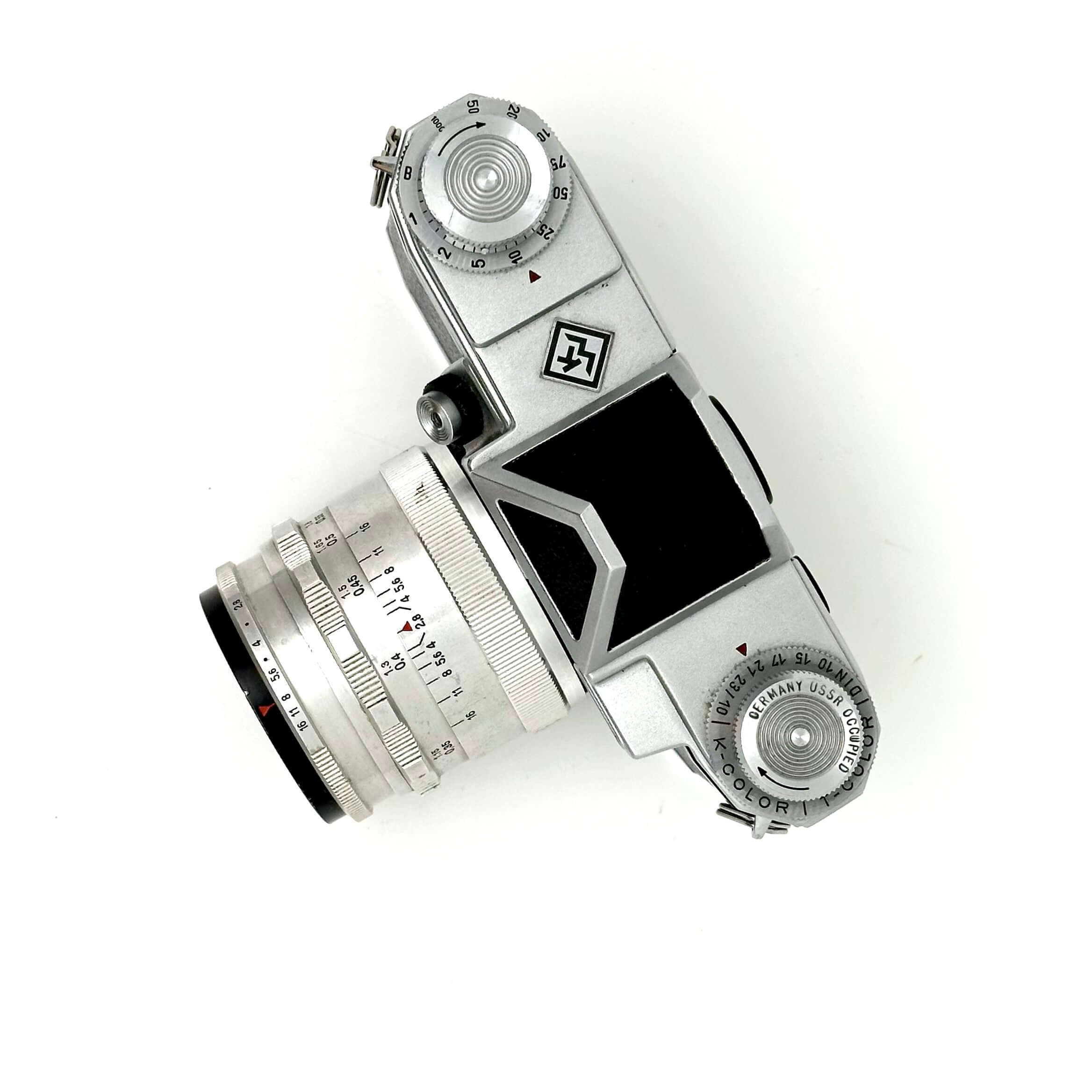 Silver-bodied vintage camera with a matching lens, featuring engraved markings and a black viewfinder window.