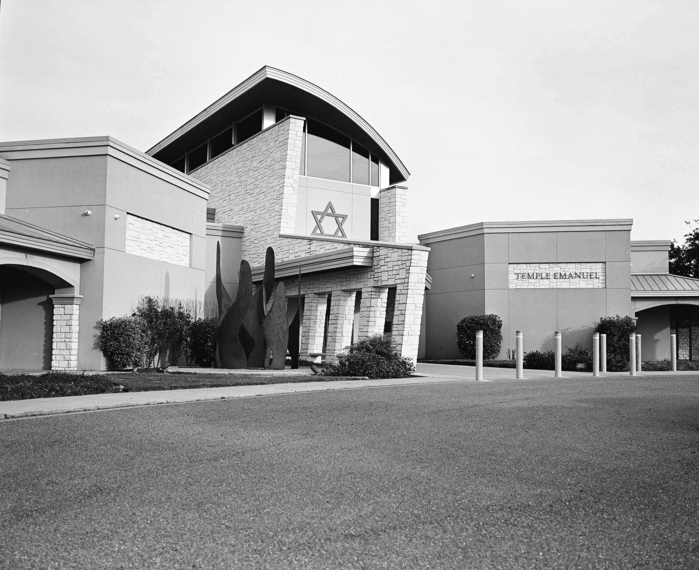 The black-and-white image shows a modern building with stone and concrete architecture, featuring an arched roofline, large windows, and a prominent star of david emblem on the facade.