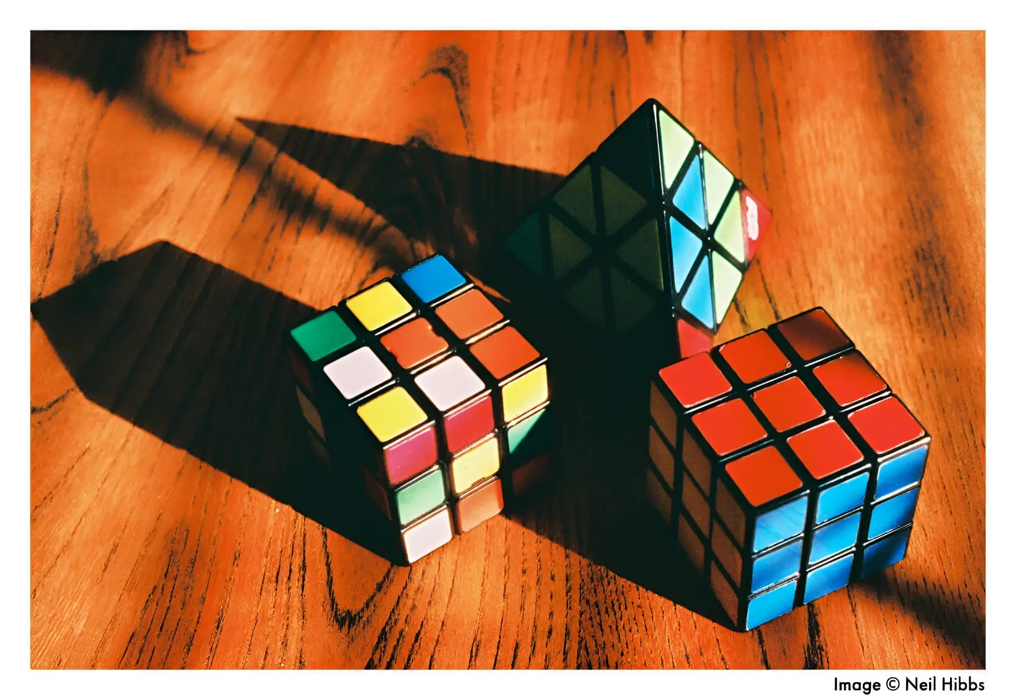 Three colorful rubik’s cubes, one solved and two partially scrambled, rest on a warm-toned wooden surface.