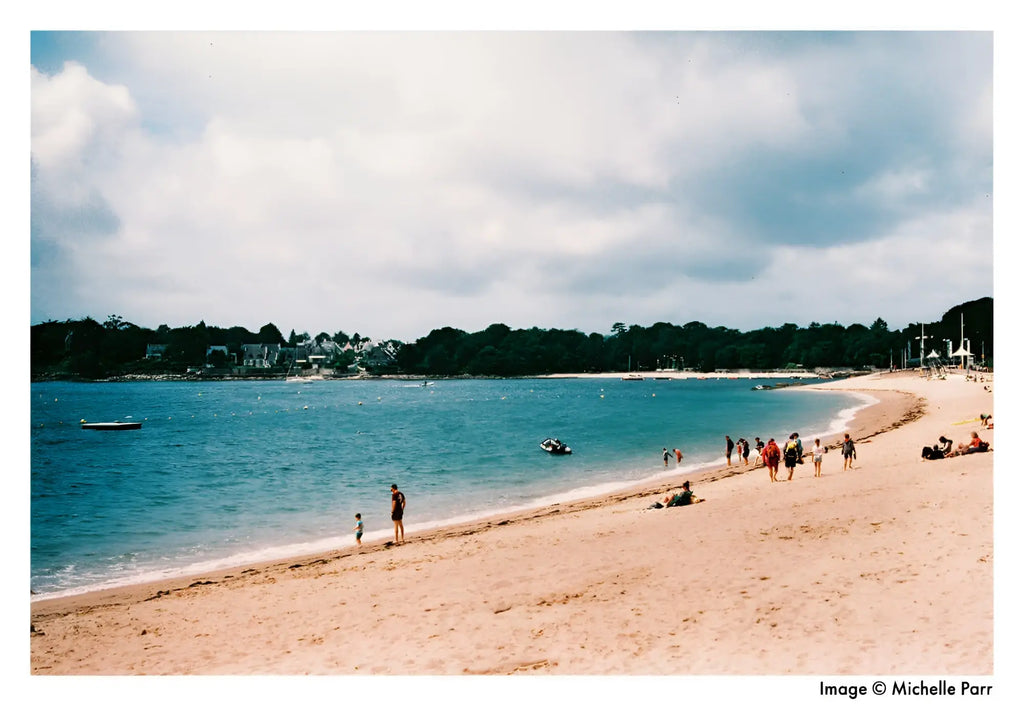 A wide, sandy beach with gentle waves lapping at the shore under a partly cloudy sky.