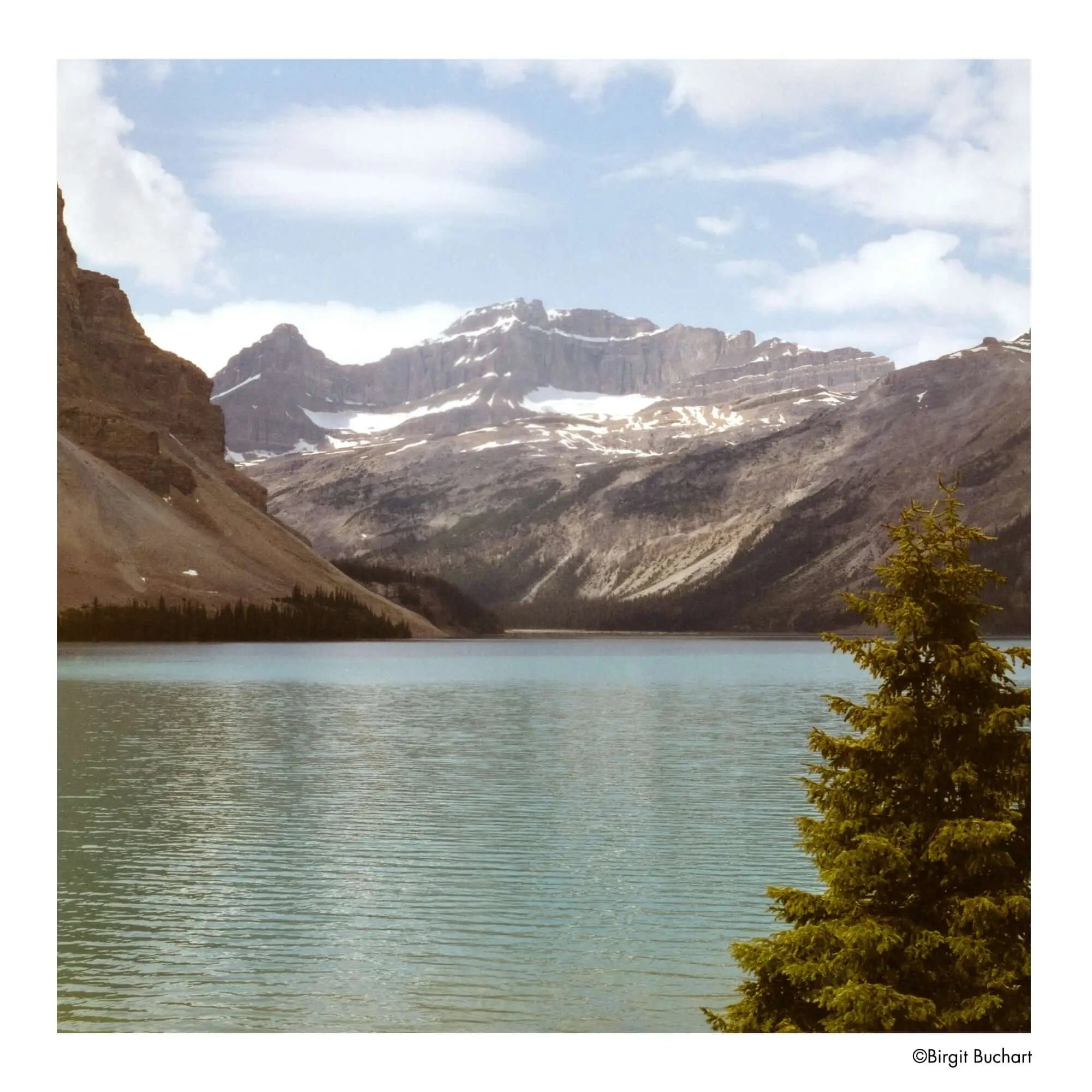 A serene turquoise lake nestled between rugged, snow-dusted mountains under a partly cloudy sky.