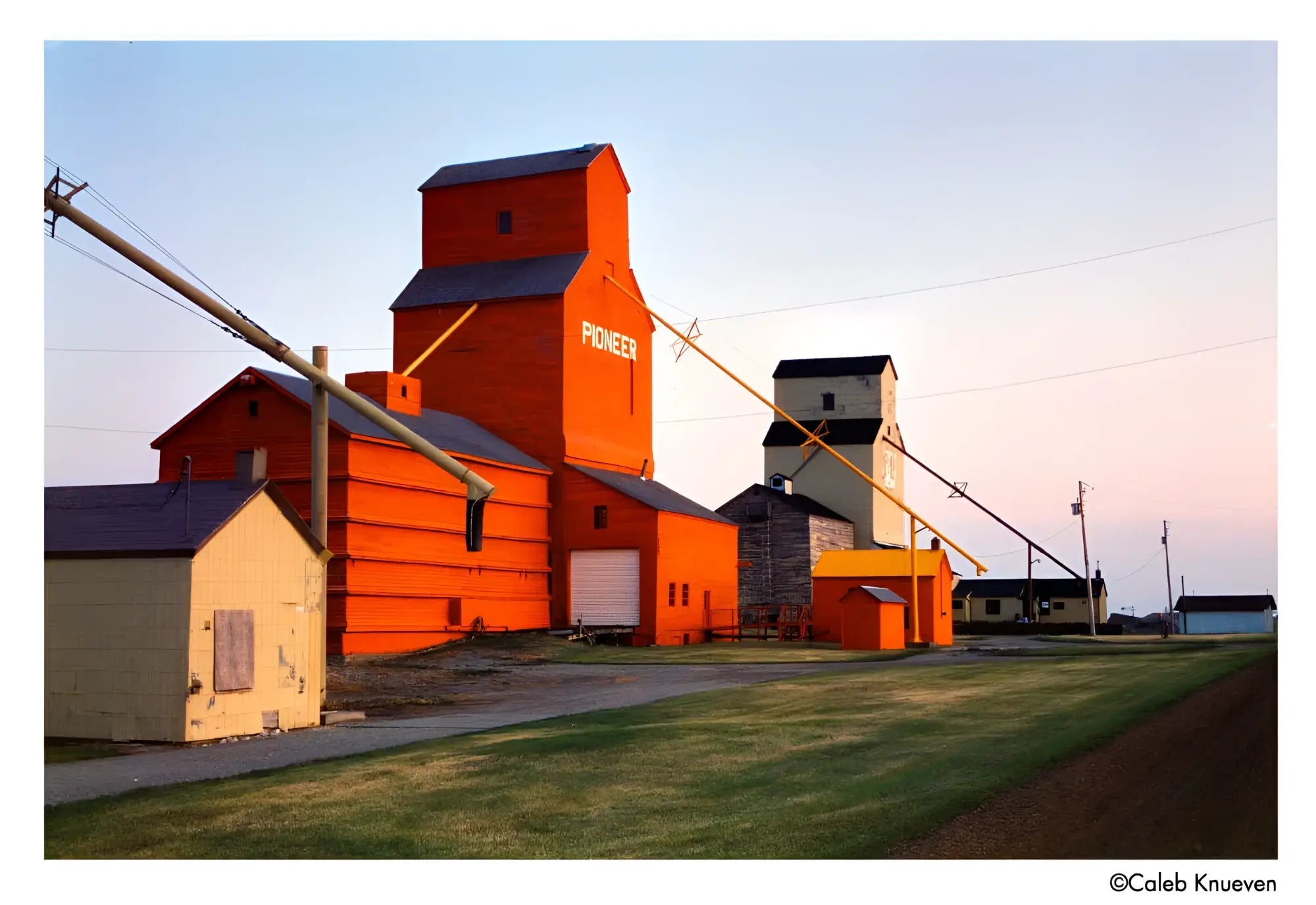 A tall, vibrant orange grain elevator with a dark gray roof and the word ’pioneer’ painted in white on its side.