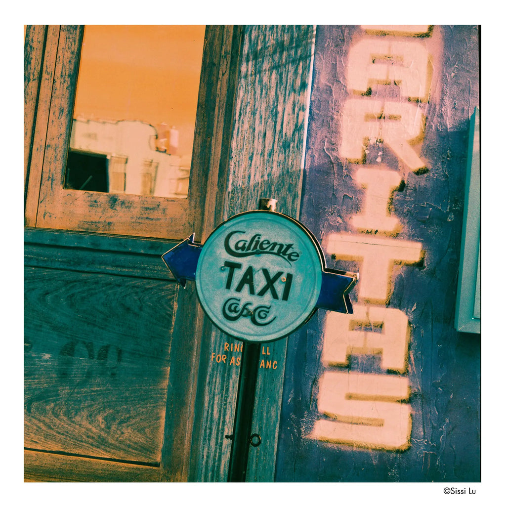 Circular teal-colored ’cafiente taxi’ sign with black lettering and a blue arrow pointing left.