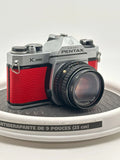 Silver and red asahi pentax k1000 film camera with textured leather grip.