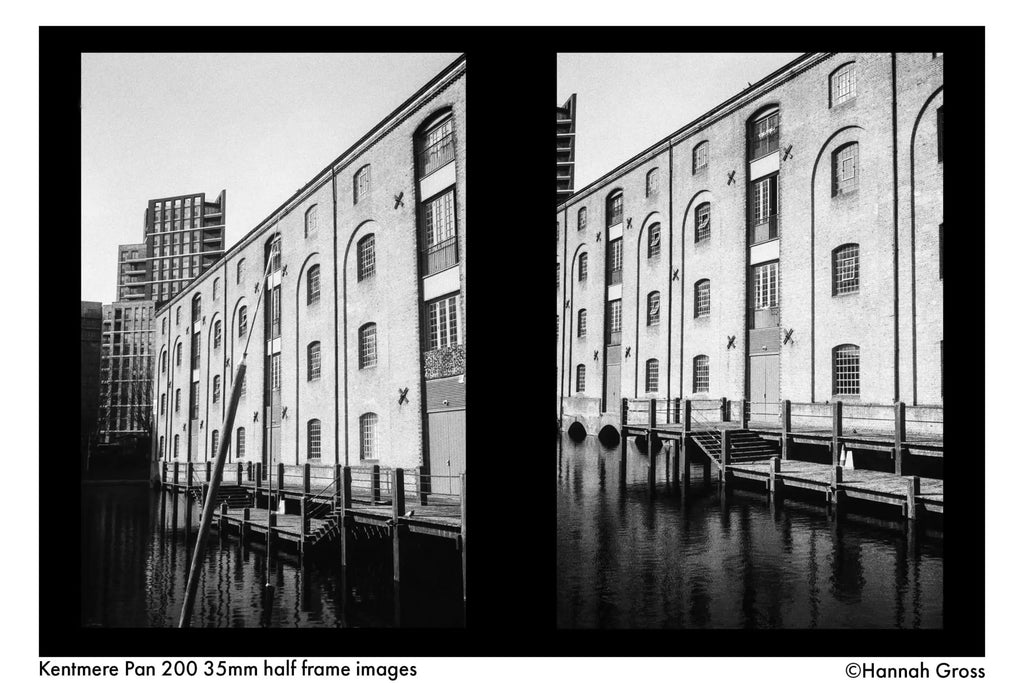 Black-and-white photograph of a historic brick warehouse building with arched windows and wooden docks along the water.