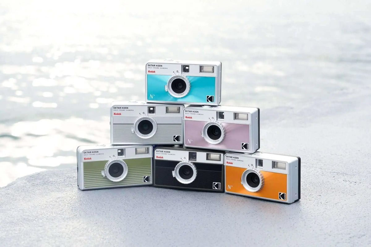 A stack of six kodak instamatic n instant cameras in assorted vibrant colors including teal, silver, pink, green, black, and orange.