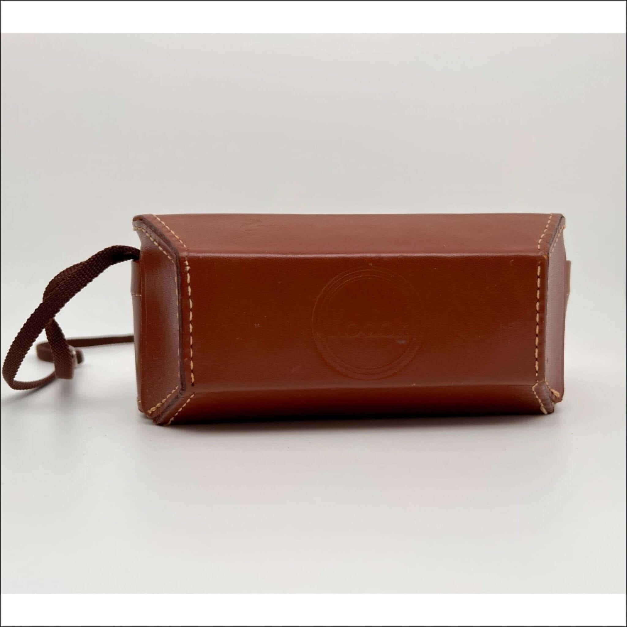 Brown leather camera case with a matching fabric strap and light-colored stitching.