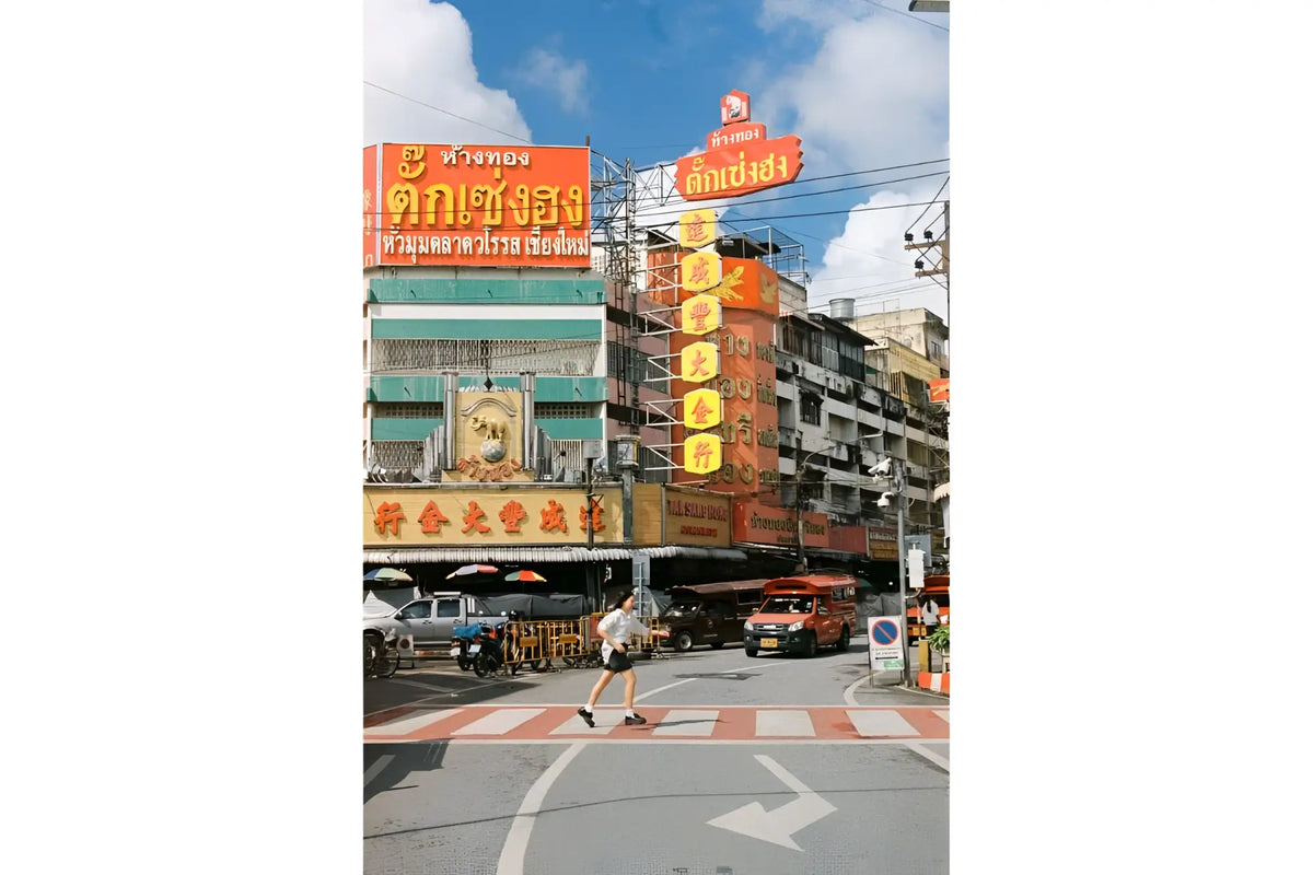 The image features a vibrant orange neon sign with thai script, mounted on the side of a multi-story building in an urban setting.
