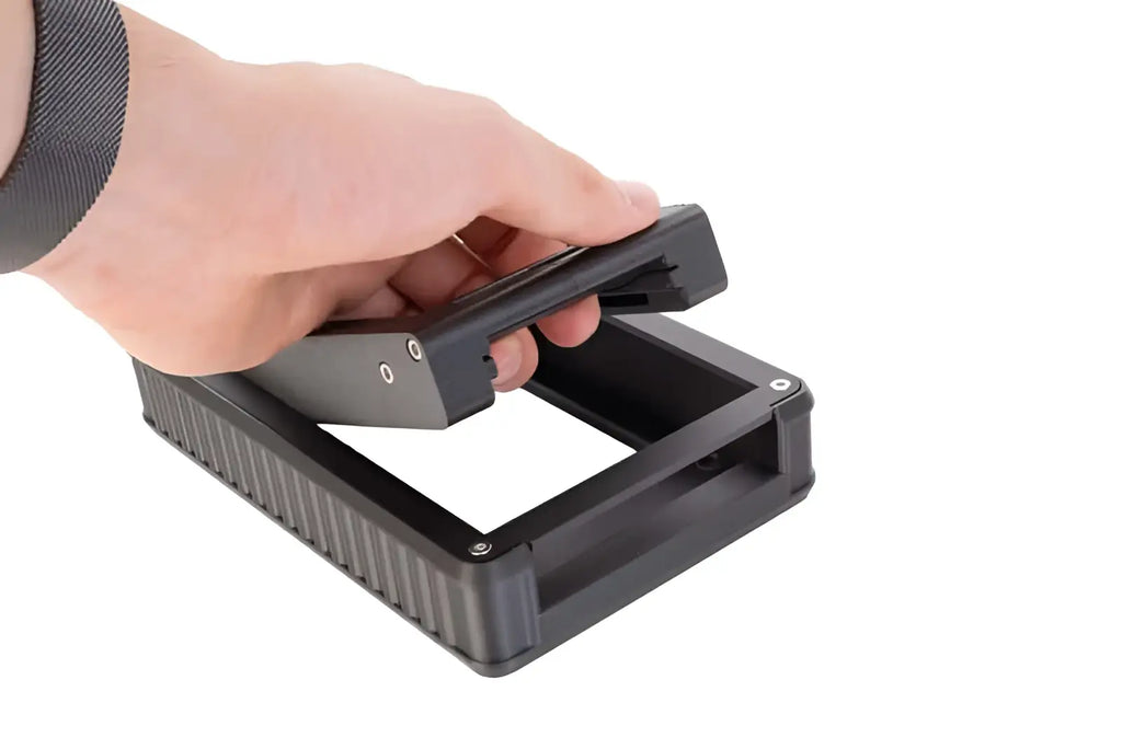 Black plastic device with textured sides and a hinged lid being held open by hand