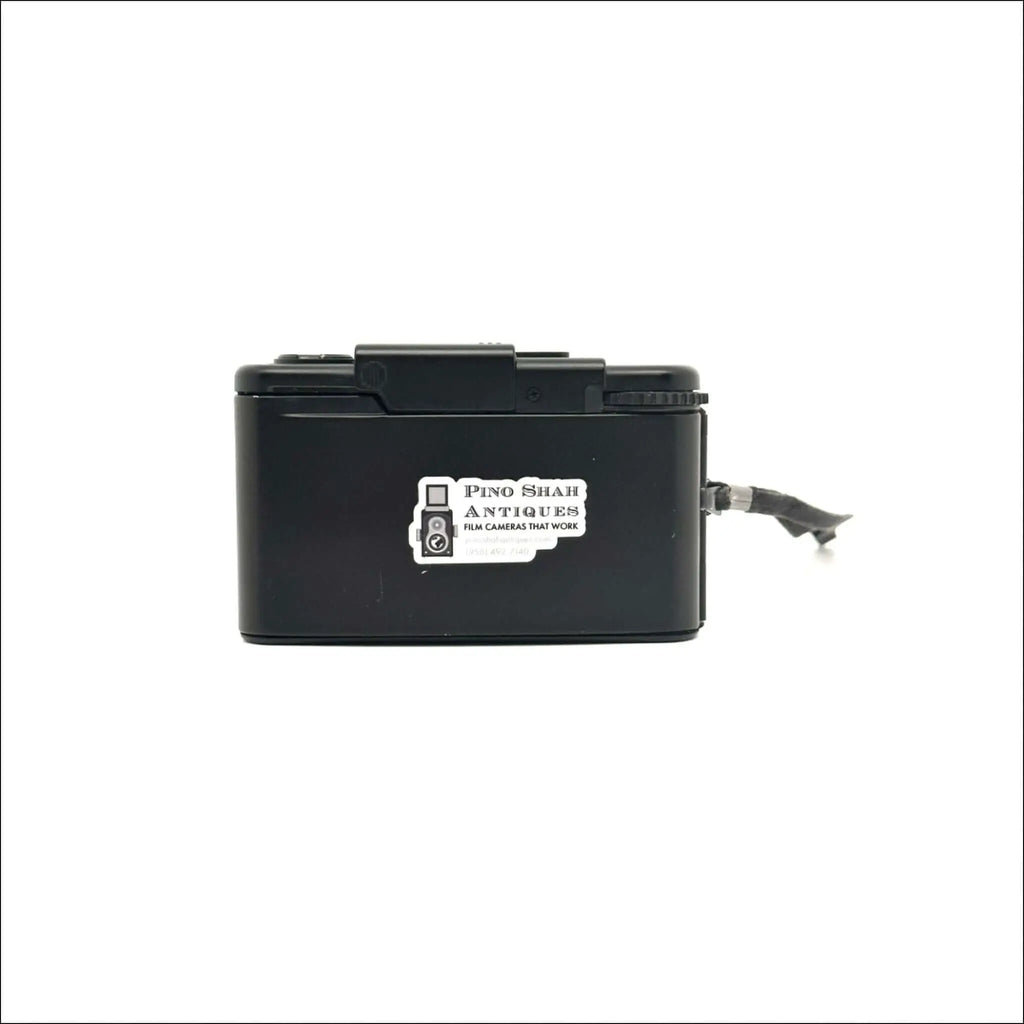 Black plastic box camera with a white sticker reading ’pino shar antiques film cameras that work’ on its side.