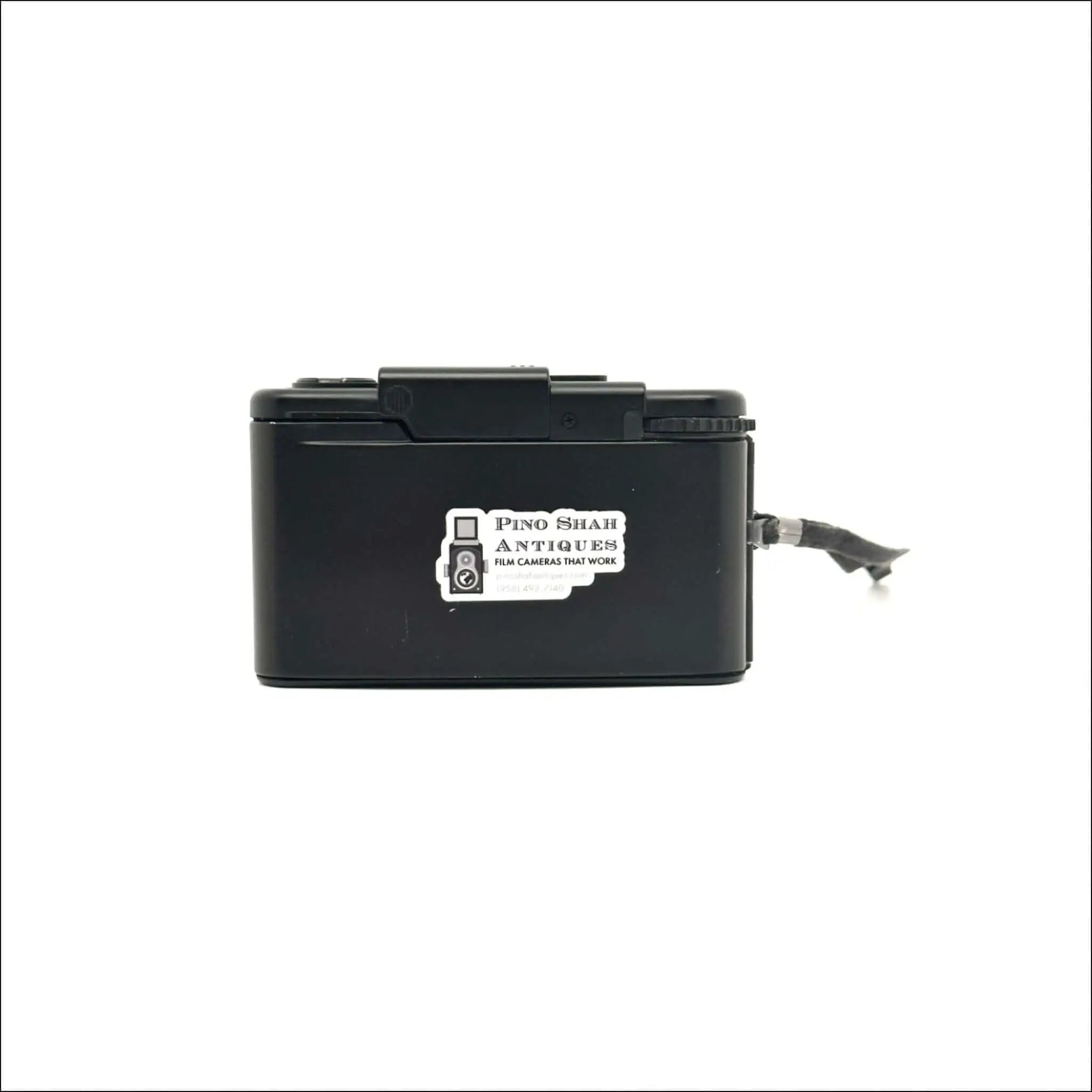 Black plastic box camera with a white sticker reading ’pino shar antiques film cameras that work’ on its side.