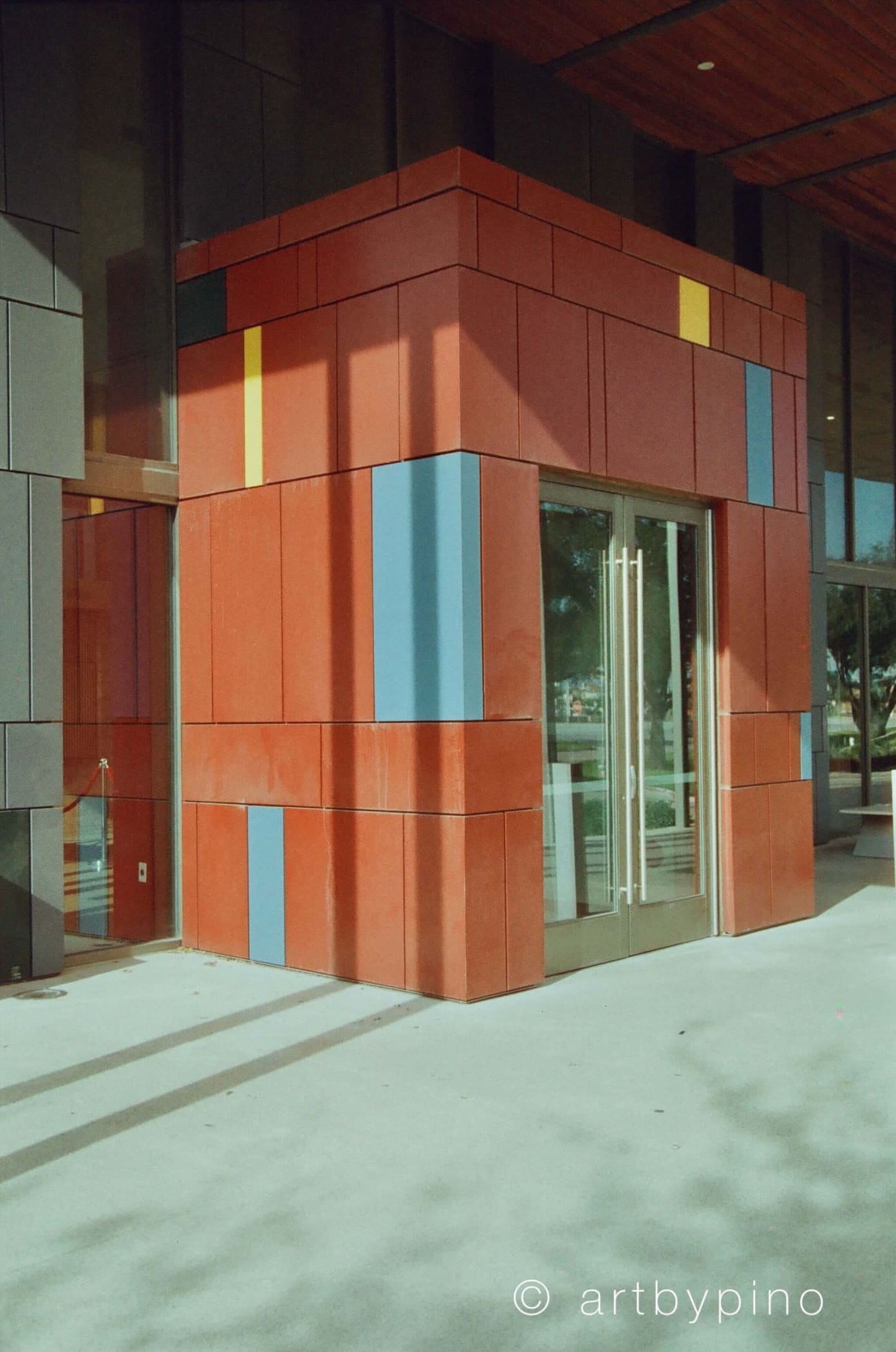 The building features a bold, geometric facade with reddish-orange panels accented by vertical stripes of yellow and blue.