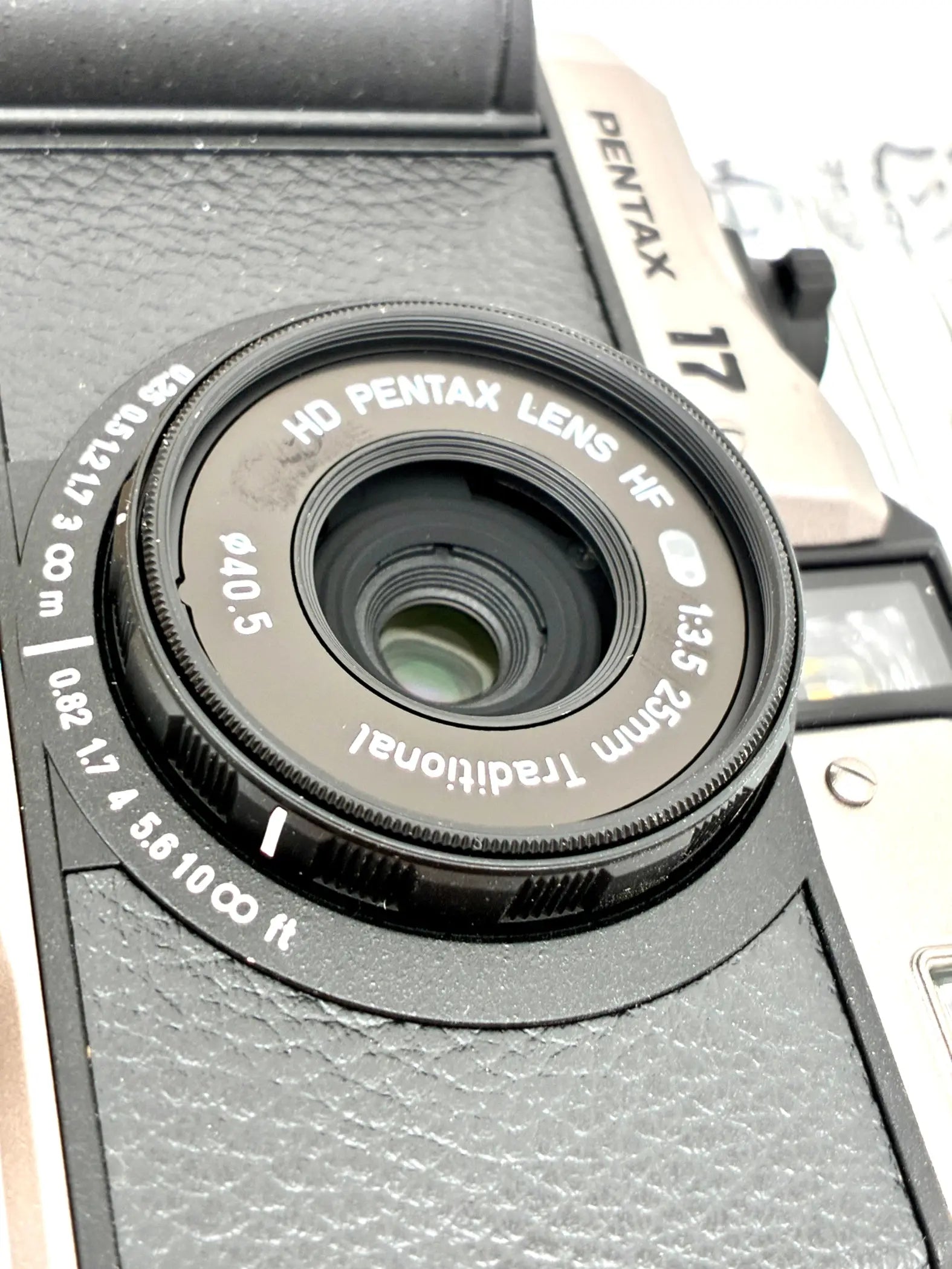 Black hd pentax hf 25mm f3.5 lens with textured grip mounted on pentax 35mm half-frame film camera body open-box