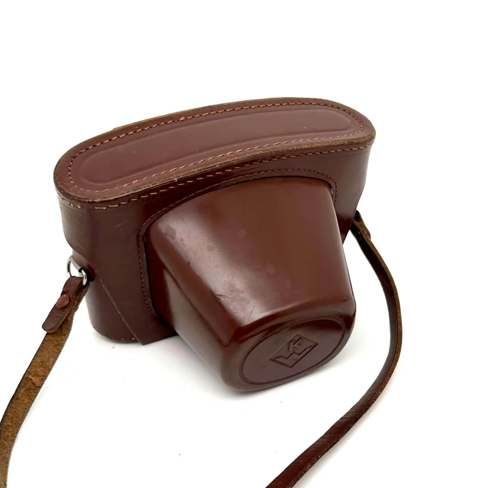 Brown leather camera case with stitched edges and a matching strap.