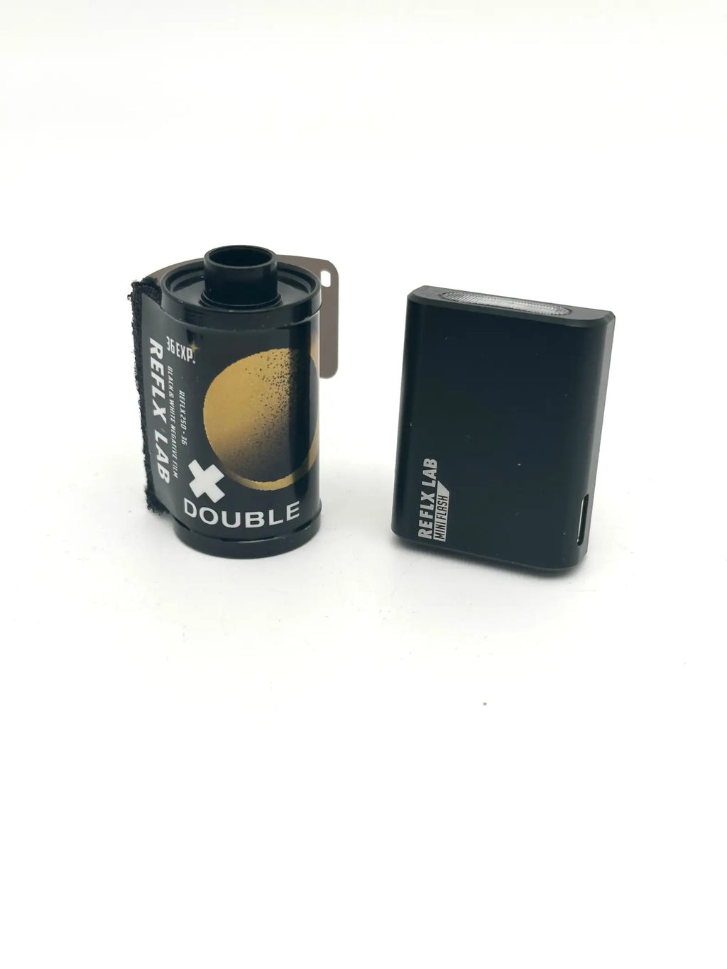 Black reflex lab double film canister with gold circular design and a matching black rectangular battery pack.