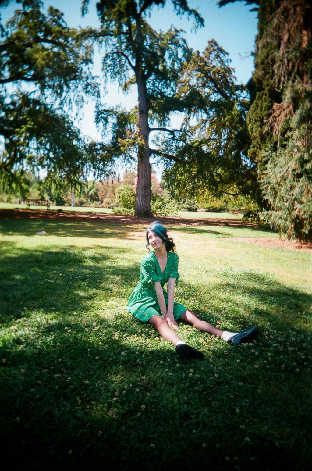 A woman in a vibrant green, short-sleeved dress with a v-neckline sits on the grass.