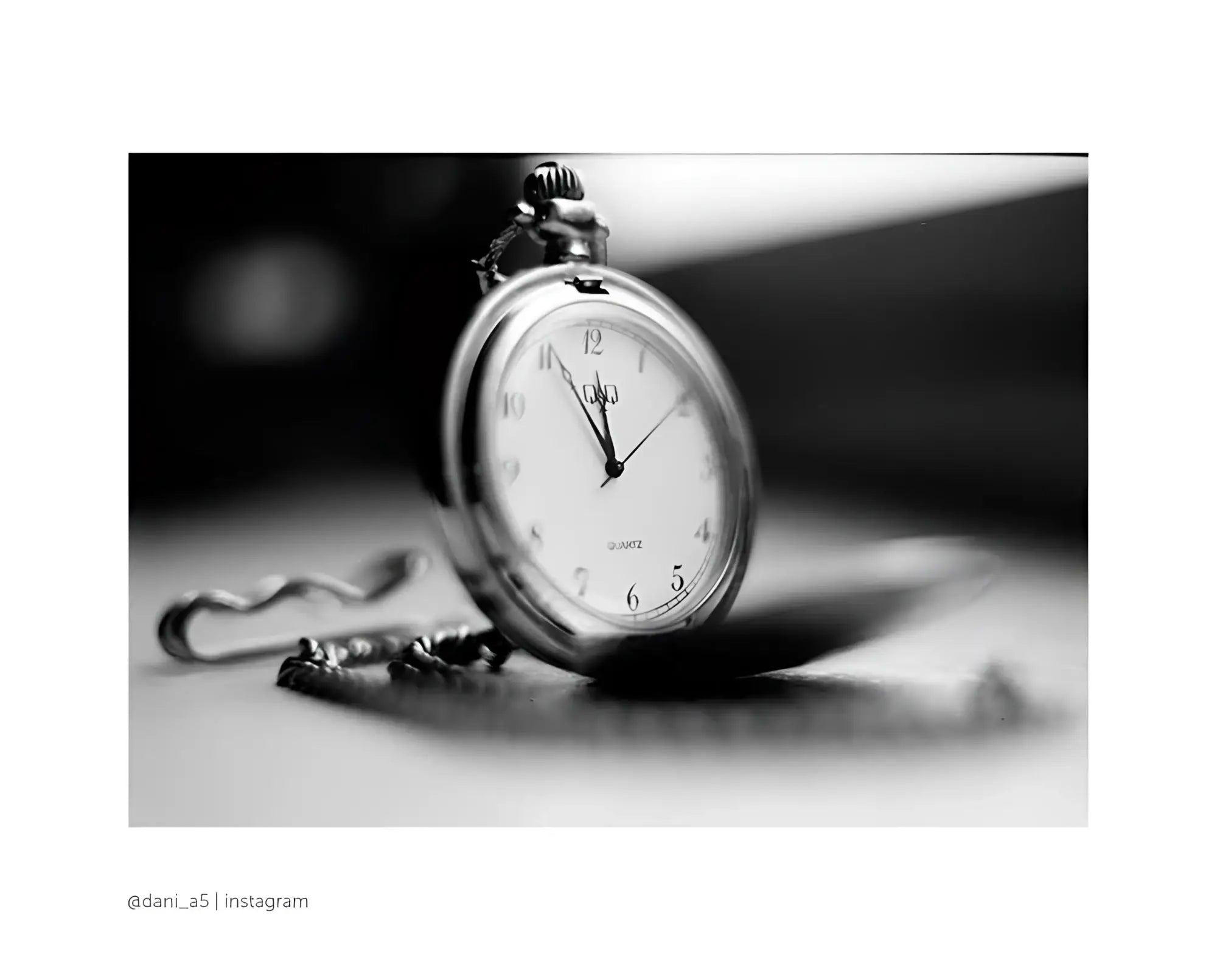 Silver-toned pocket watch with a classic round face, white dial marked by black numerals and hands, attached to an ornate chain.