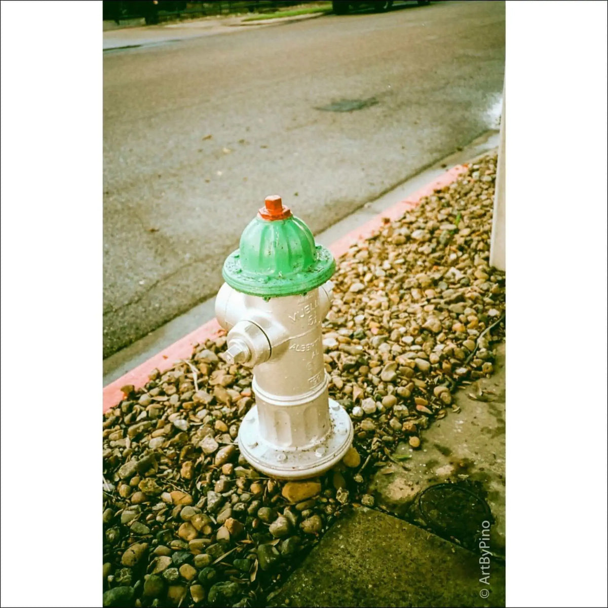 A green and silver fire hydrant on a pebbled sidewalk by the street, showcasing urban infrastructure.