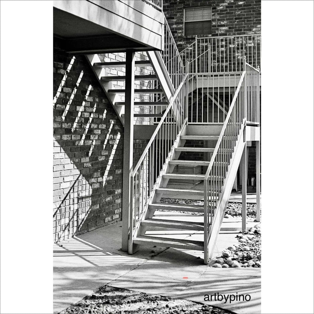 Metallic staircase with vertical railings and concrete steps against a brick wall