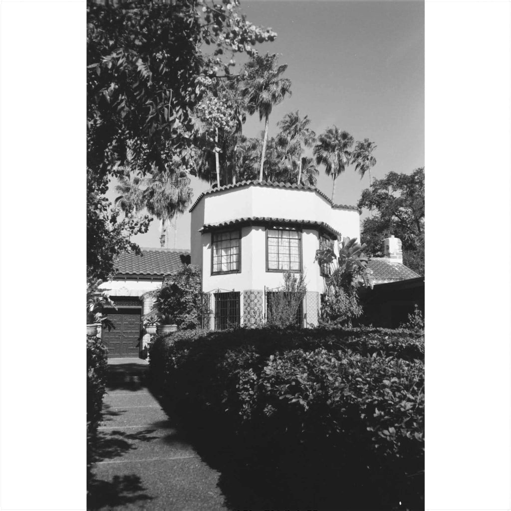 Black and white photo of a house surrounded by lush greenery and palm trees.